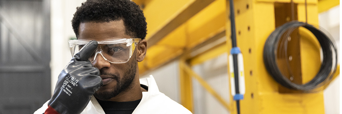 An engineeer in protective workwear pushes safety goggles up his nose as he smiles into the camera